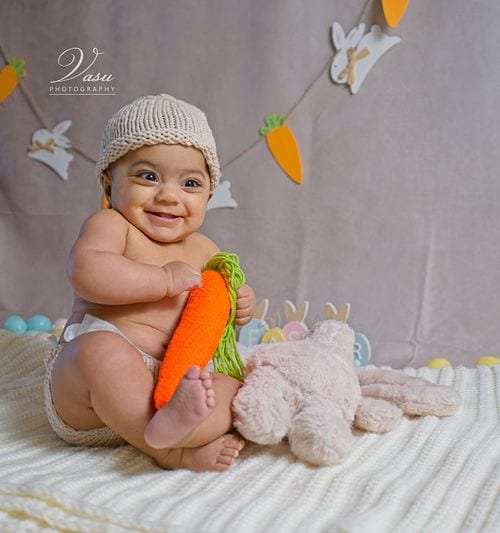 Smiling baby holding a knitted carrot during a studio portrait