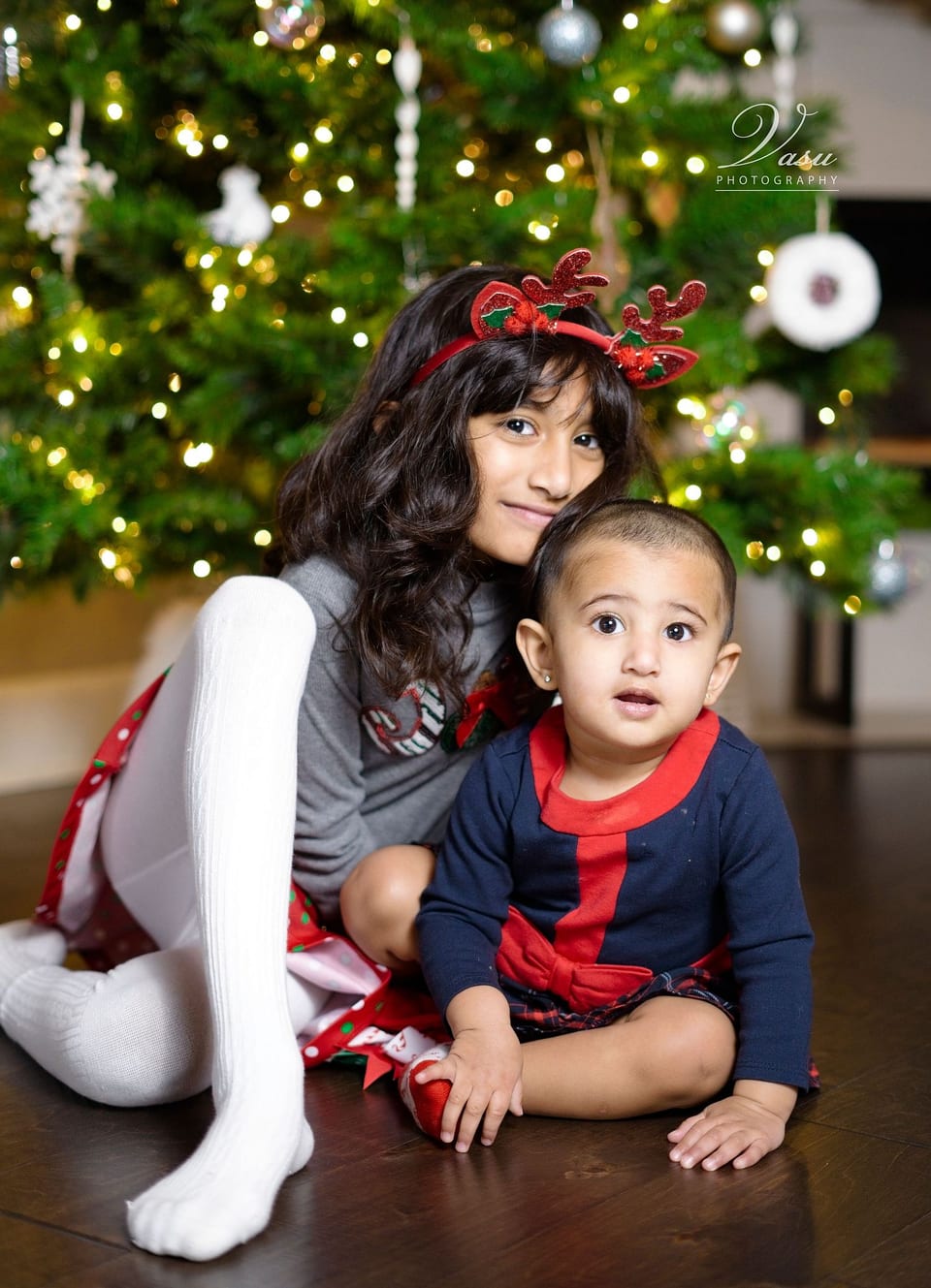 Two children photographed together in front of holiday lights