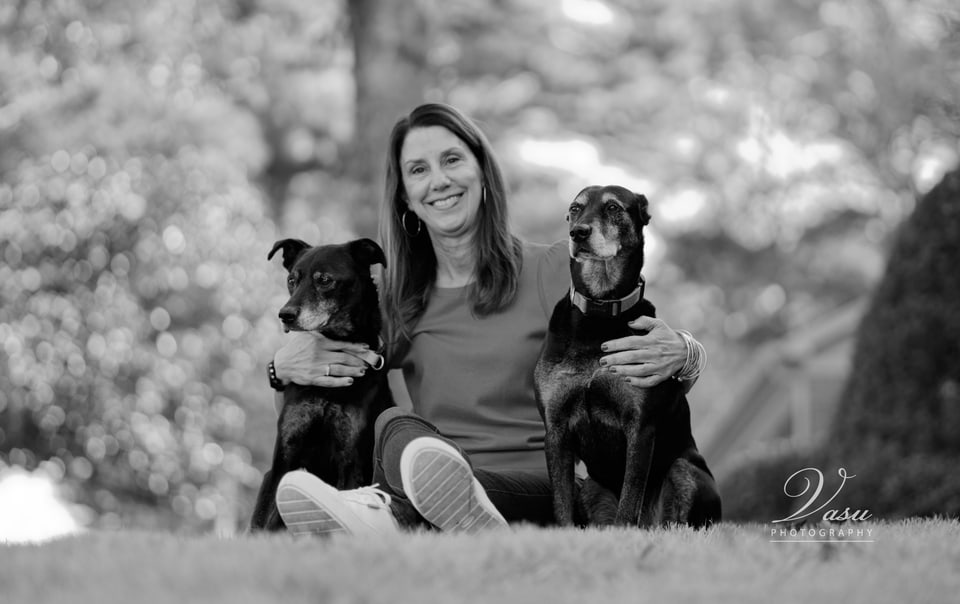 Black-and-white environmental portrait of a woman relaxing outdoors with two dogs